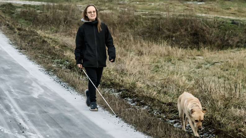 En tjej med vit käpp är ute och går med sin hund